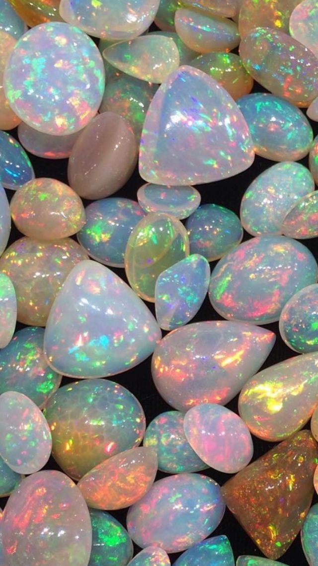 A collection of polished opals in various shapes and sizes, displaying vibrant iridescent colors such as blue, green, yellow, and pink, against a dark background.