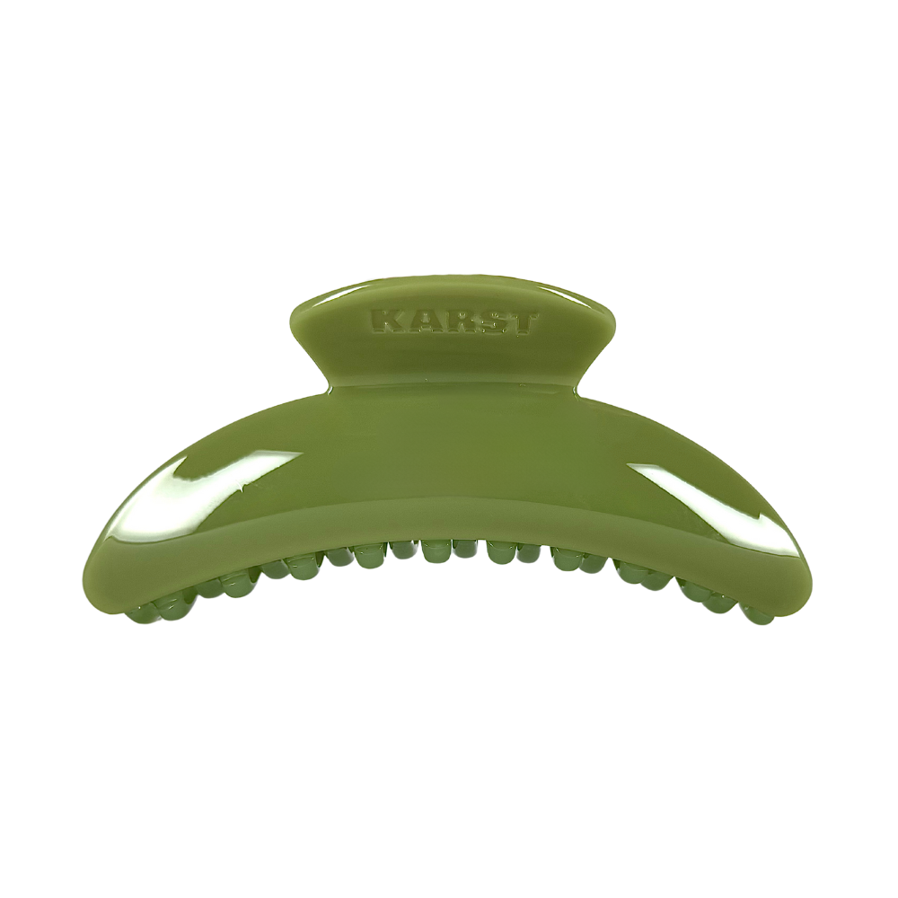 The Karst Essentials Slim Hair Claw Clip in olive is a glossy, curved accessory ideal for thicker hair, featuring "KARST" embossed on top and shown against a plain white background.
