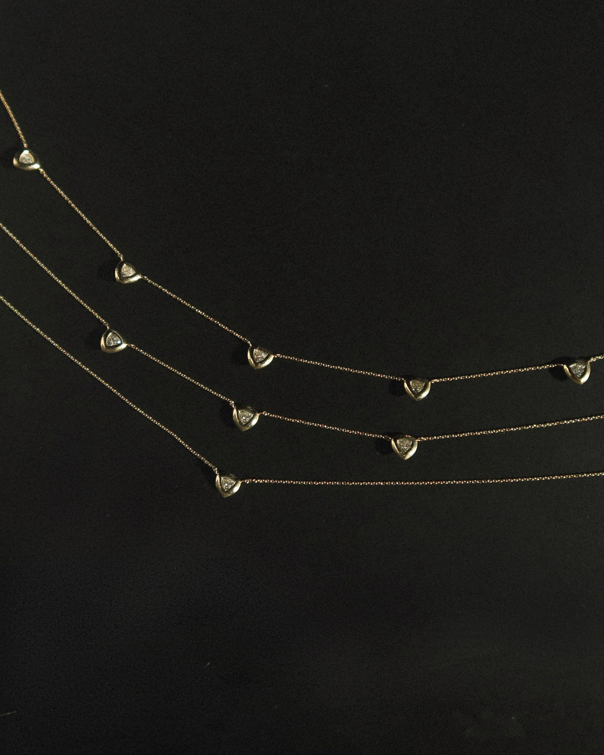 Three delicate gold necklaces, each adorned with evenly spaced small heart-shaped pendants, are arranged diagonally against a black background.