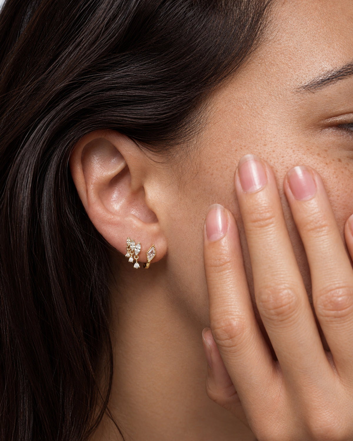 Close-up of an ear wearing a Gabby + Phoebe Set, featuring a kite huggie with a marquise-cut stone and a coordinating kite huggie with a floral cluster of small white stones.