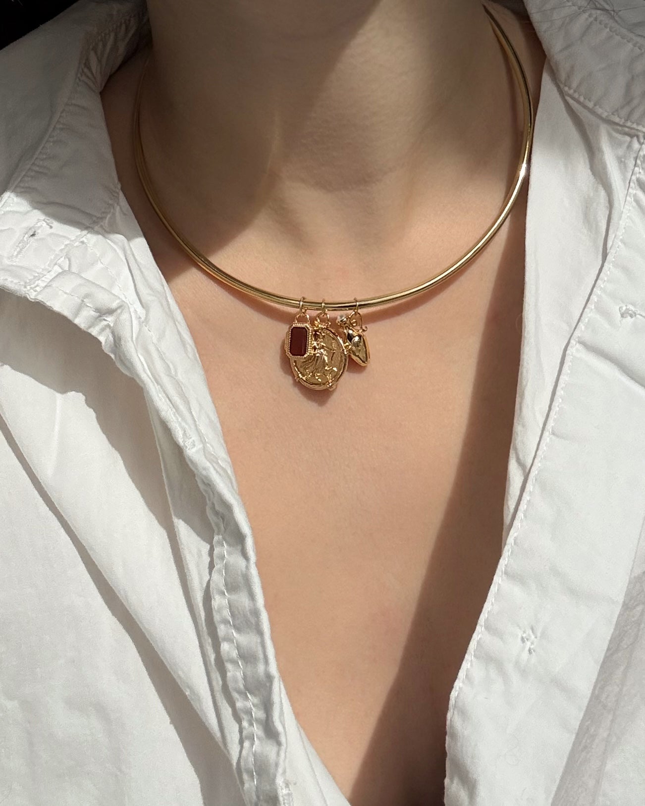 A person wears a white, partially unbuttoned shirt and a shiny Mod + Jo Mabel Rectangle Birthstone Locket Charm, a 14k gold plated choker necklace featuring interchangeable gemstone pendants.