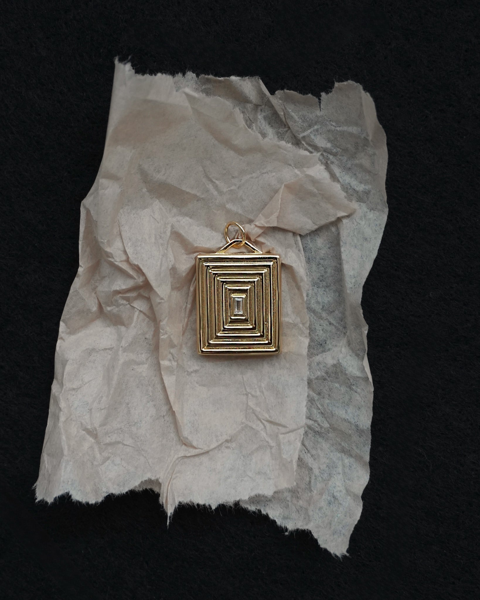 Gold pendant on crumpled white paper against a black background