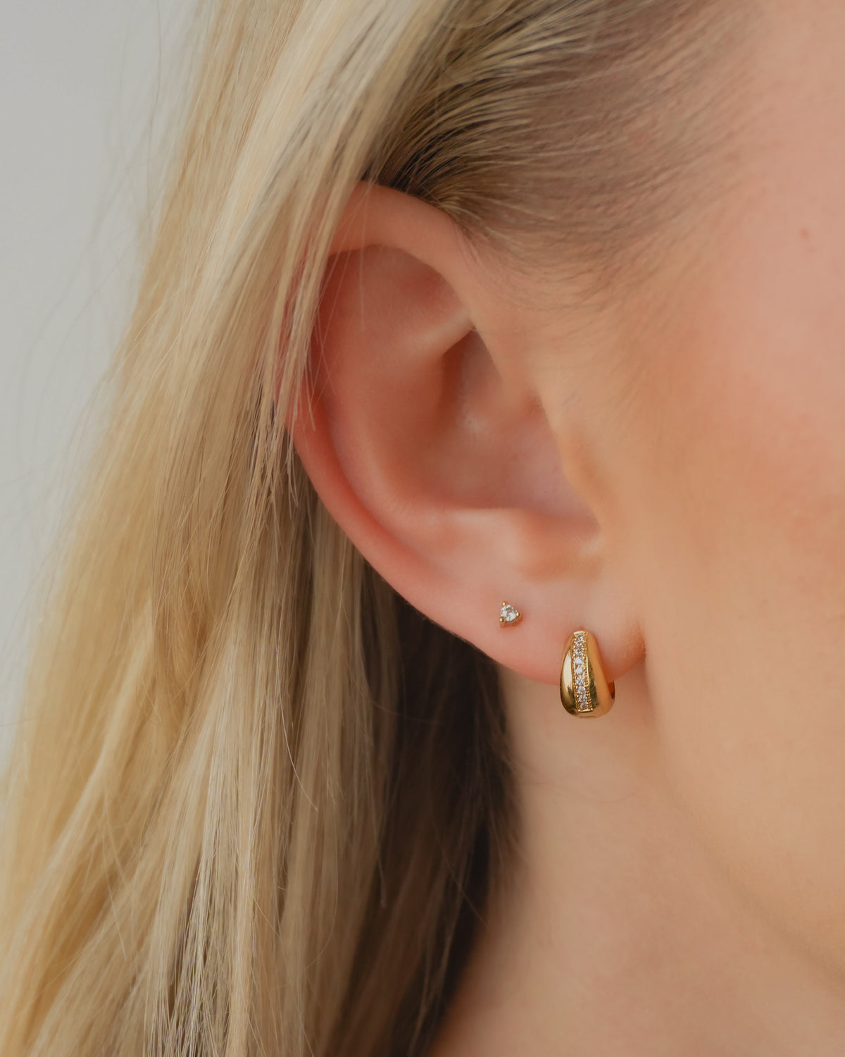 The Brianne + Ace Set featuring a chunky gold huggie hoop earring with a row of small stones and a matching single-stone stud earring on an earlobe.