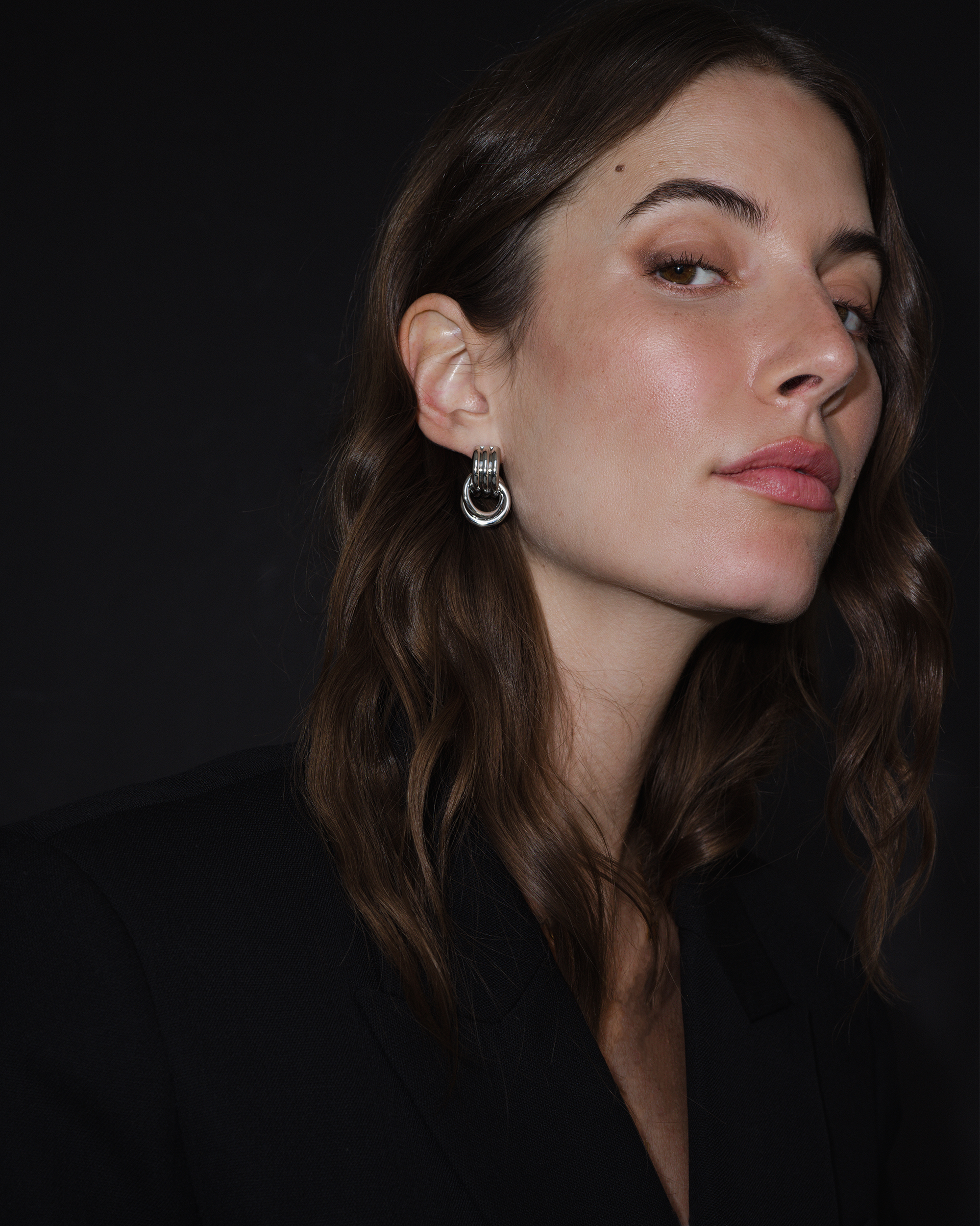 Woman wearing a silver earring against a dark background