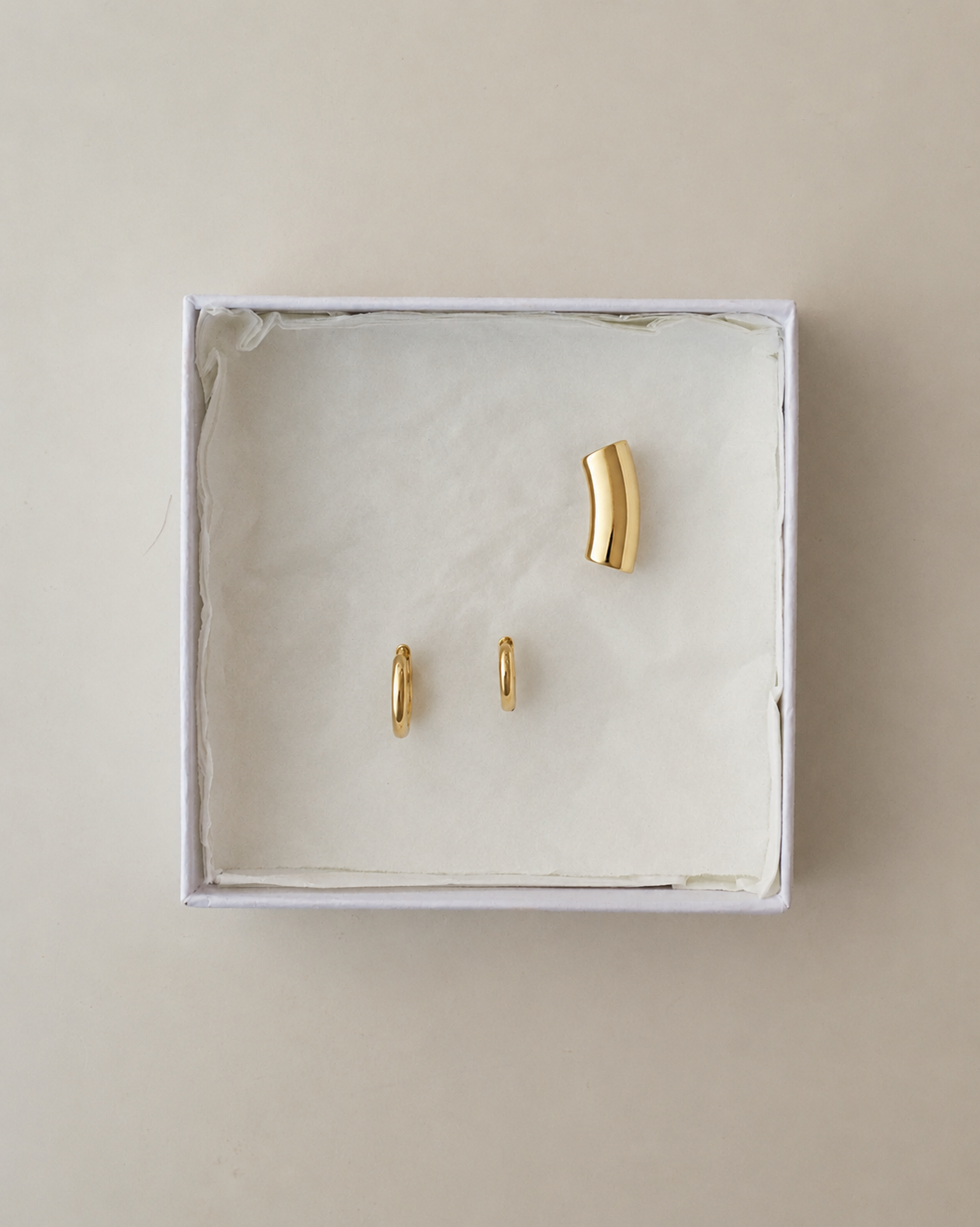 The Reneé + Lennon Set featuring two small gold huggie earrings and a curved gold ear cuff inside a white gift box.