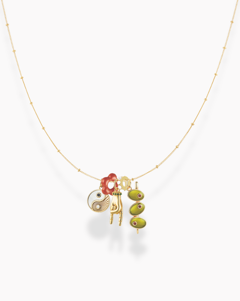 A delicate gold necklace featuring several pendants, including a yin-yang charm, red and gold rings, a gold letter H, and two green oval beads with eye motifs.