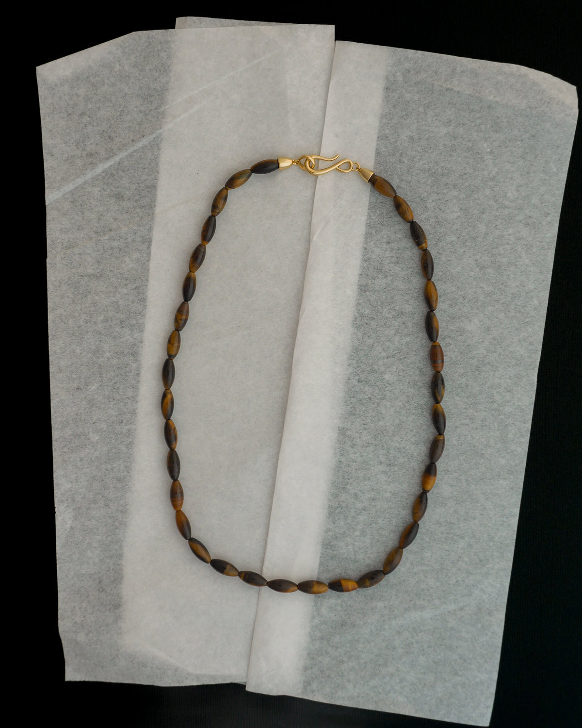 Sutton Gemstone Necklace featuring an 18″ strand of tiger’s eye, elongated rice-shaped beads, and a gold S-hook clasp.