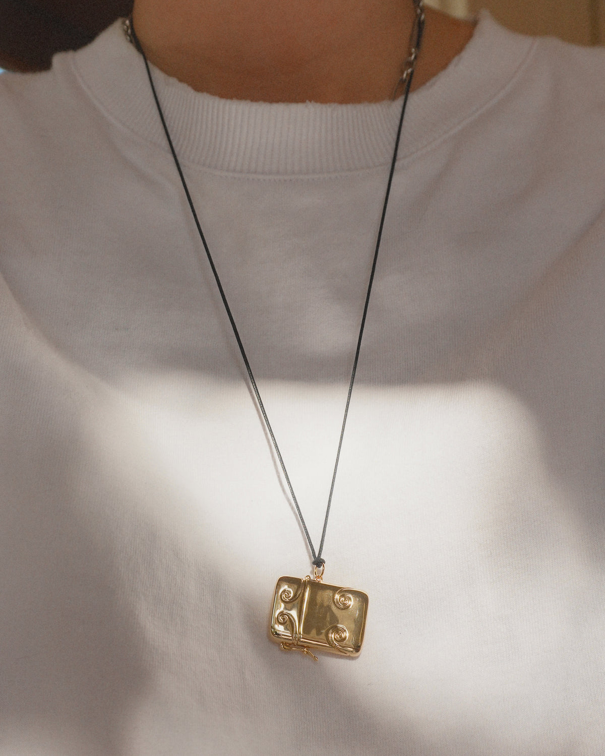 The gold-plated, book-shaped Sybil Vesta Case Charm hangs on a thin black cord in the style of Victorian jewelry.