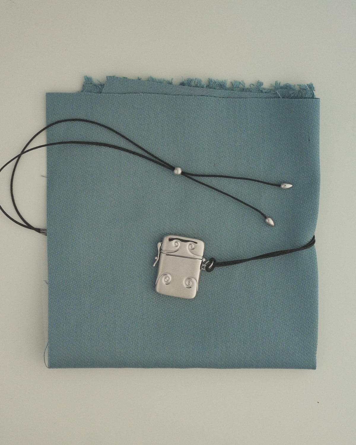 Sybil Vesta Case Charm: a silver rectangular Victorian vesta case with a swivel-top design on a black cord.