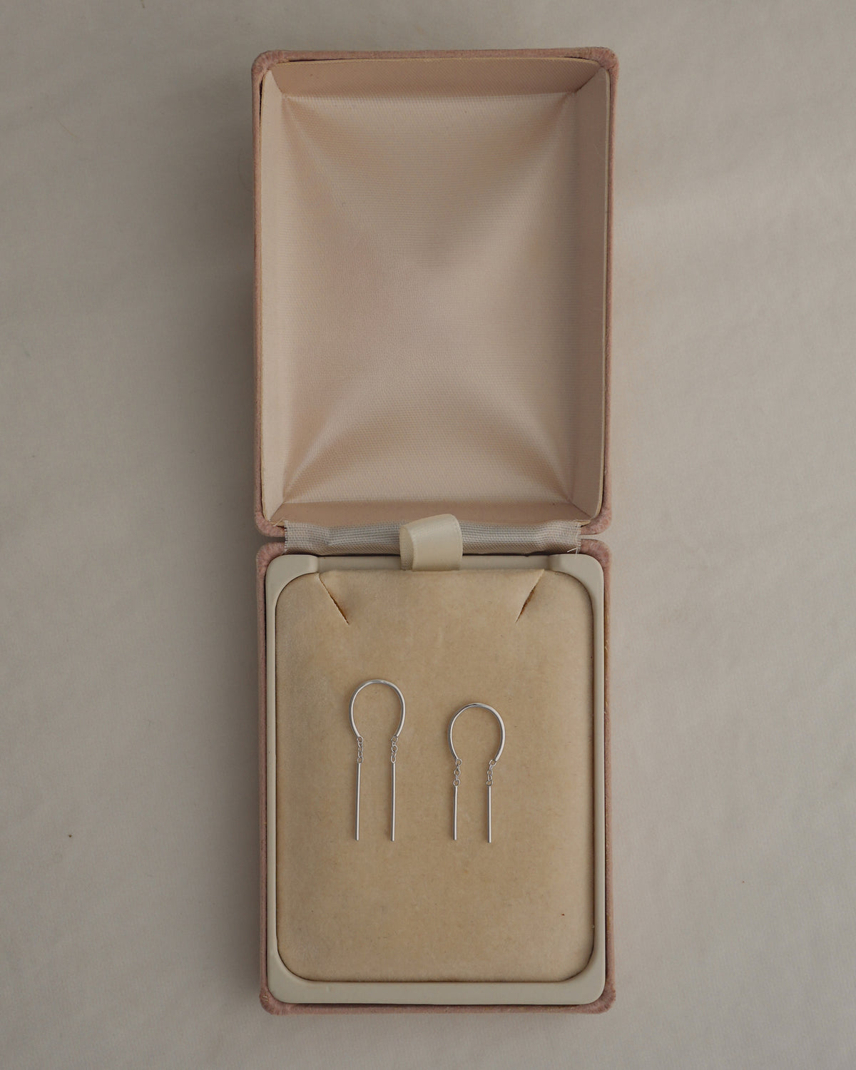 Two silver U-shaped rhodium plate Mila Smooth Threader Huggies Set earrings resting inside an open jewelry box.