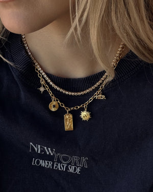 Close-up of a person wearing gold necklaces with various charms on a dark blue shirt.