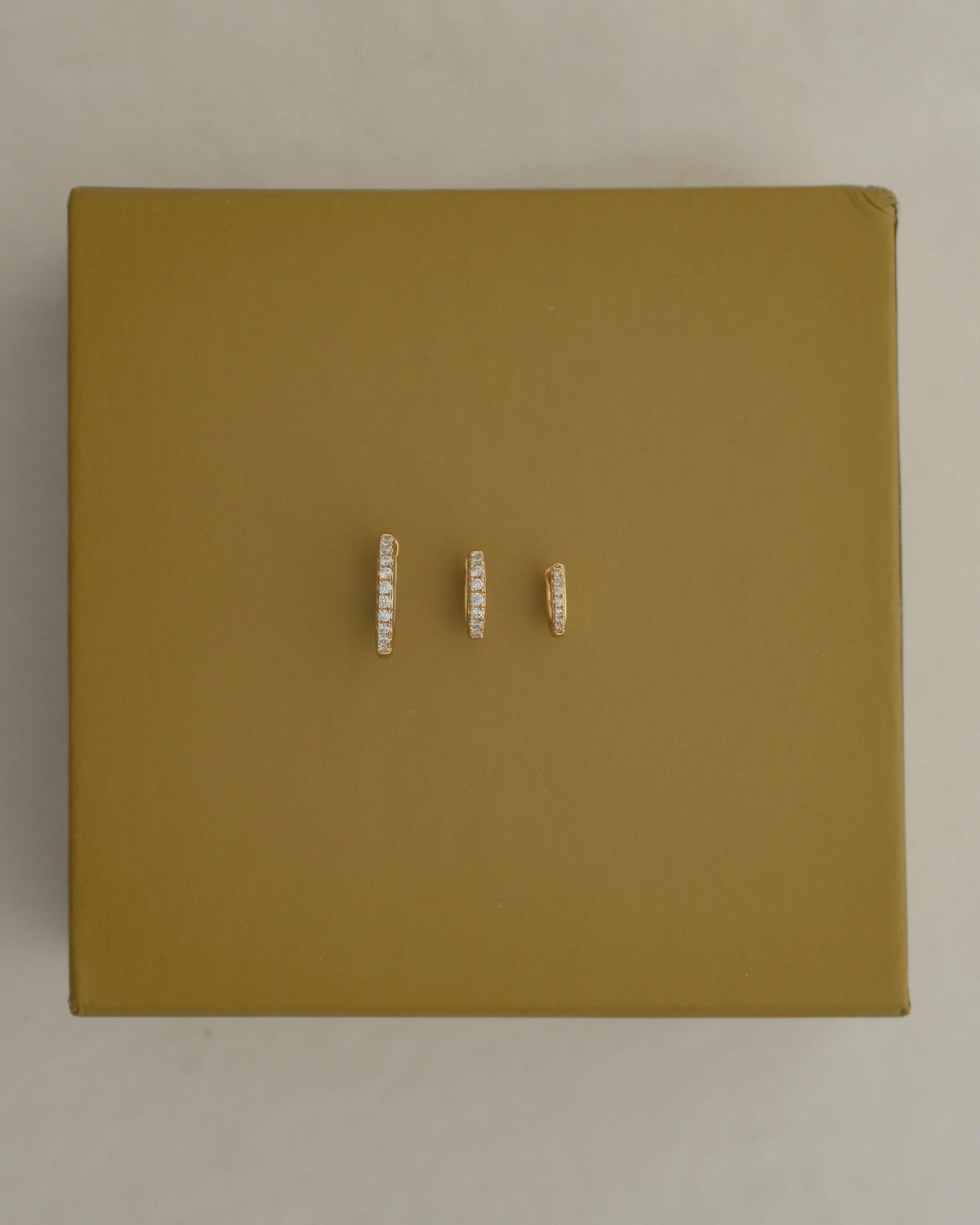 Three pavé hoop earrings from the Reese Gift Set by Mod + Jo in varying sizes, each accented with a row of small clear stones, arranged horizontally on a gold box to create an elegant ear stack.