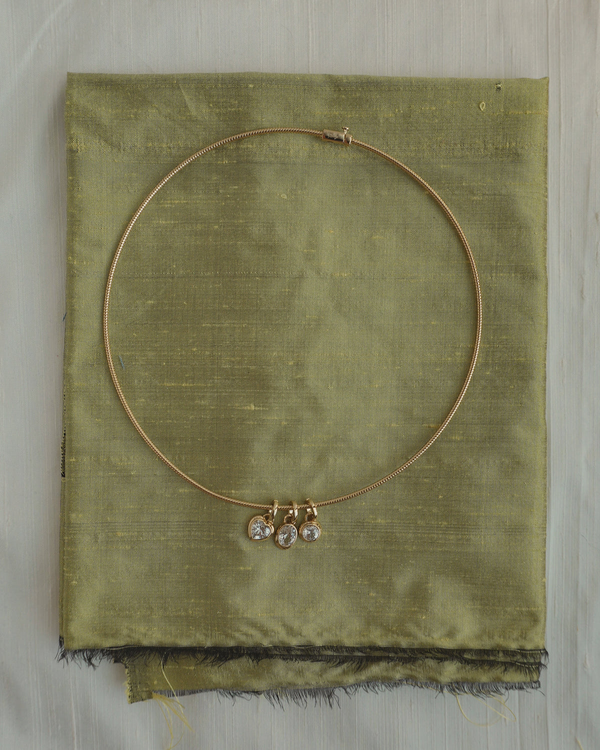 Gold-tone rigid Celine Collar Necklace by Mod + Jo with three small dangling charms featuring clear stones in heart, oval, and round shapes.