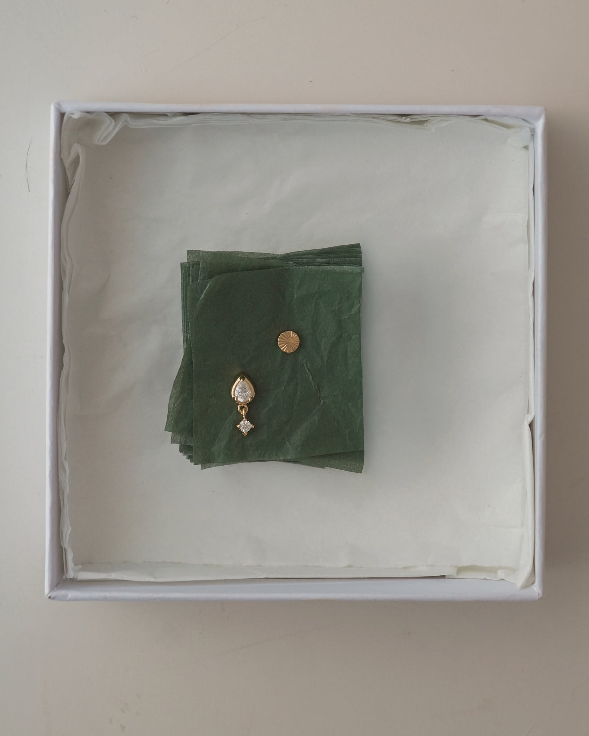 Quinn + Dela Set featuring Dela Fluted Studs and a gold teardrop pendant earring with a small inset stone, resting on a stack of green tissue paper inside a white gift box.