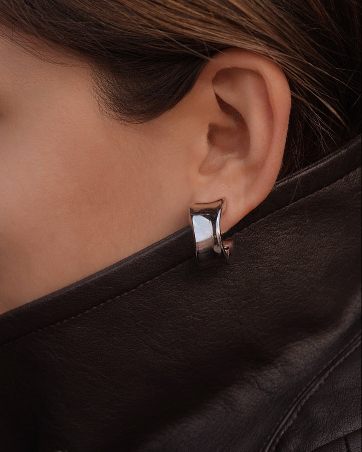Close-up of a person wearing a silver hoop earring with a dark jacket.