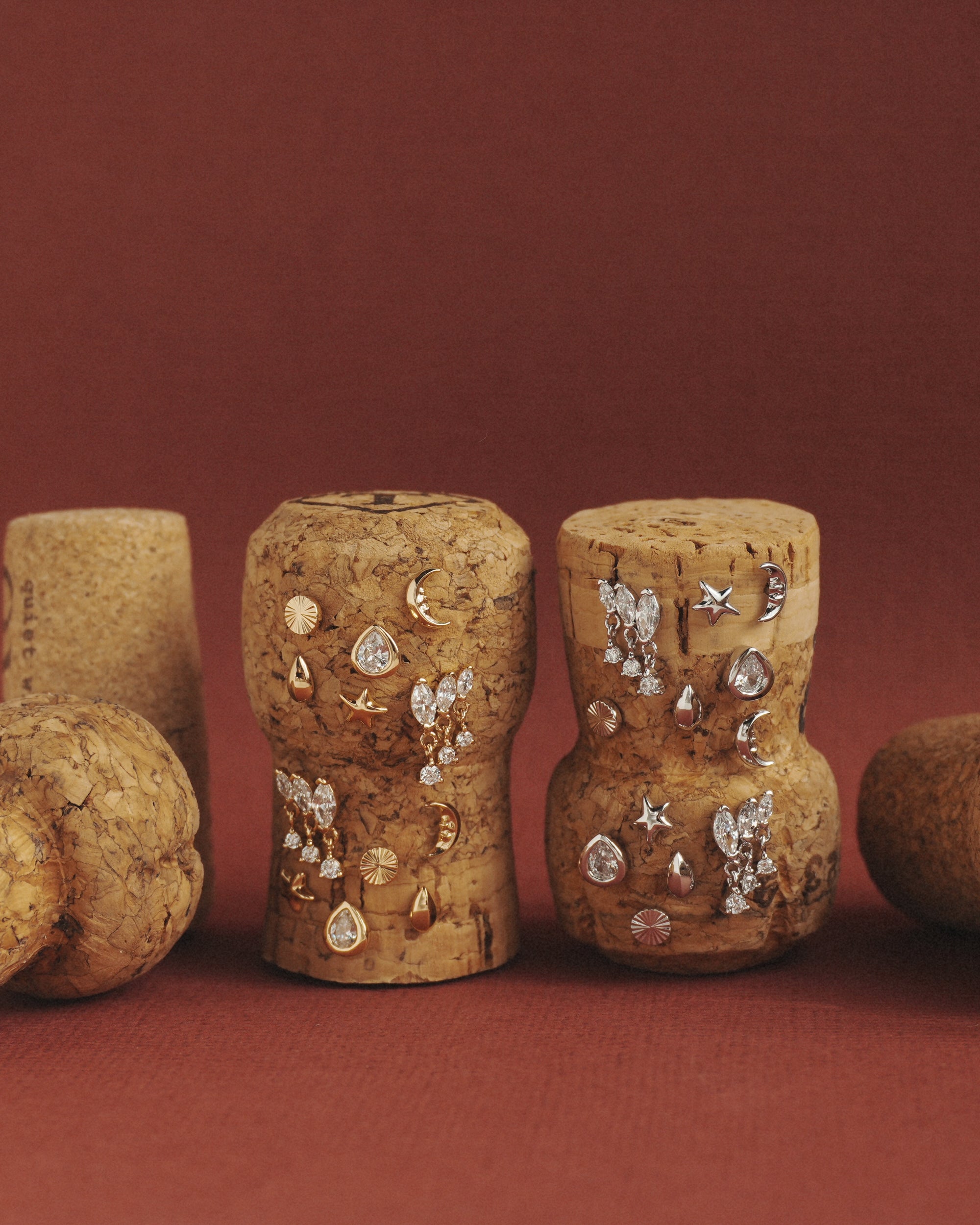 Mod + Jo’s Gabby Marquise Dangle Studs, alongside other cubic zirconia earrings in various designs, are displayed on champagne corks against a reddish-brown background.