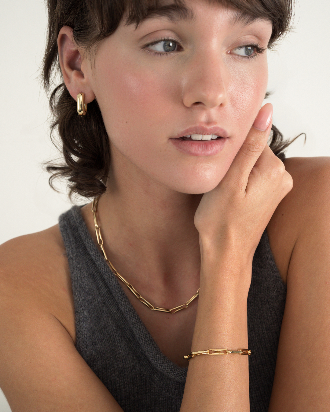 A person wearing the Barely-There Trio Set by Mod + Jo, featuring petite gold hoop earrings, an elongated link chain necklace, and a matching gold chain-link bracelet.