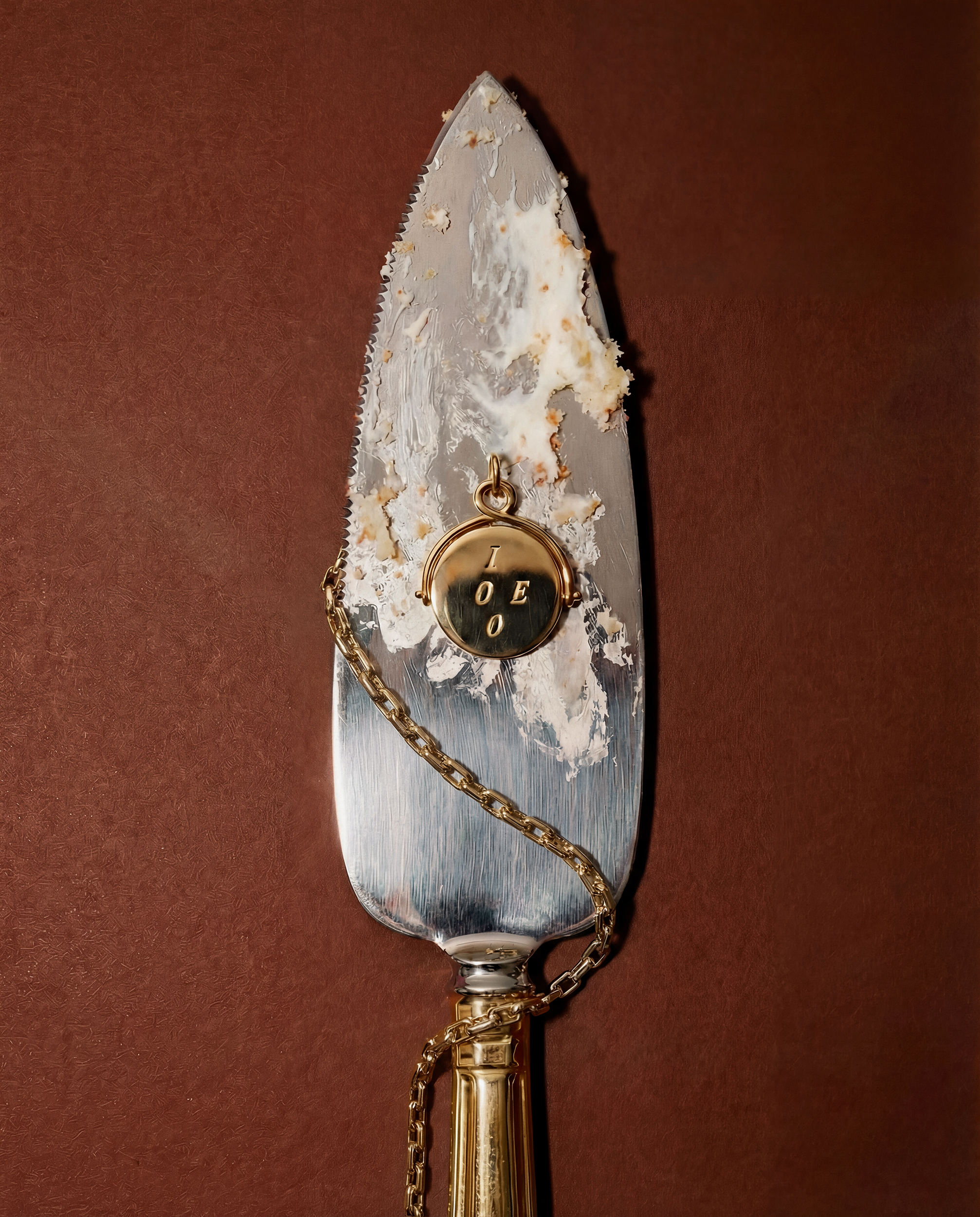 Decorative cake server with a metallic blade and gold handle on a brown background with a gold charm and chain draped on it.