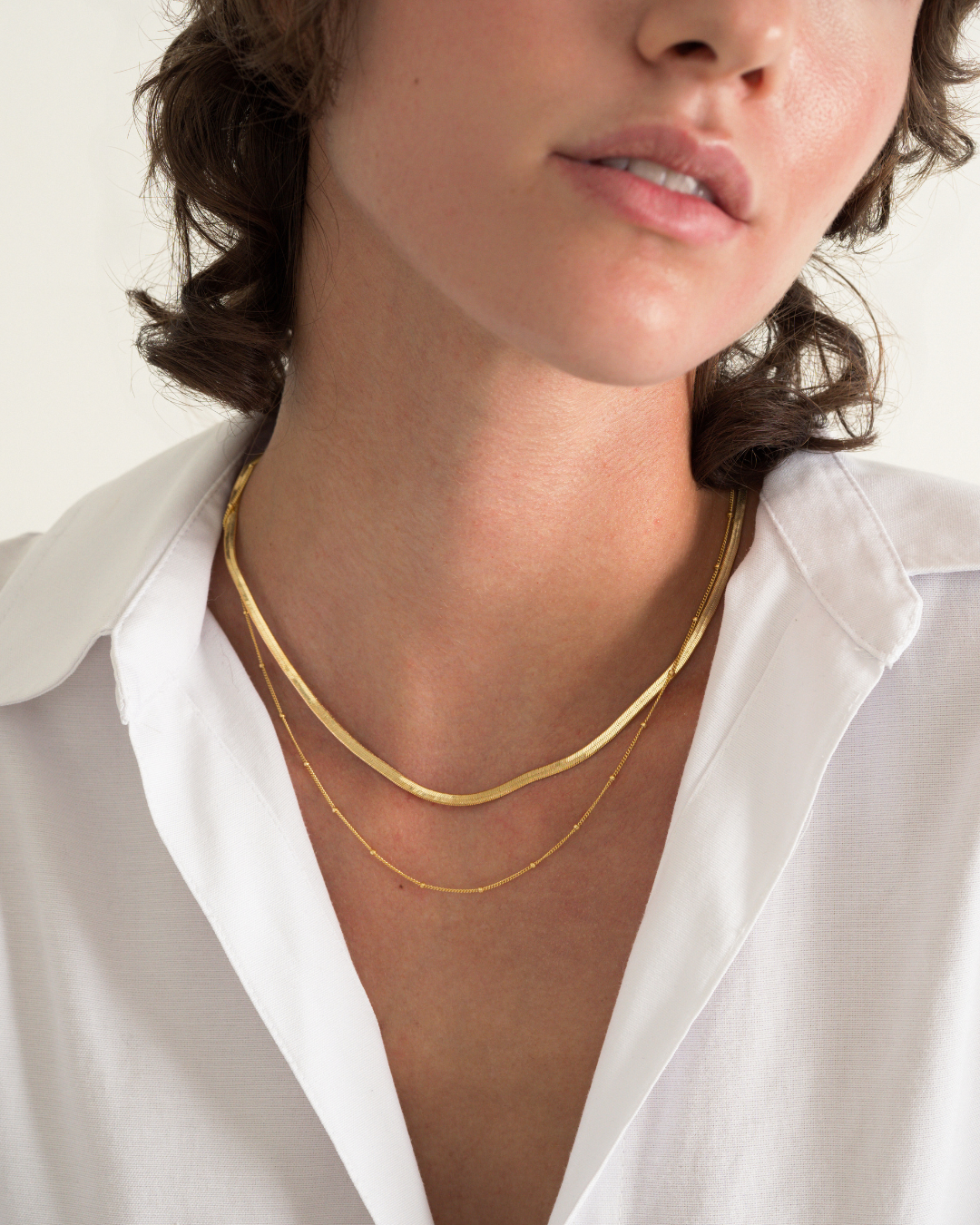 A person wearing the Everyday Necklace Set, consisting of a flat herringbone chain and a delicate satellite chain.