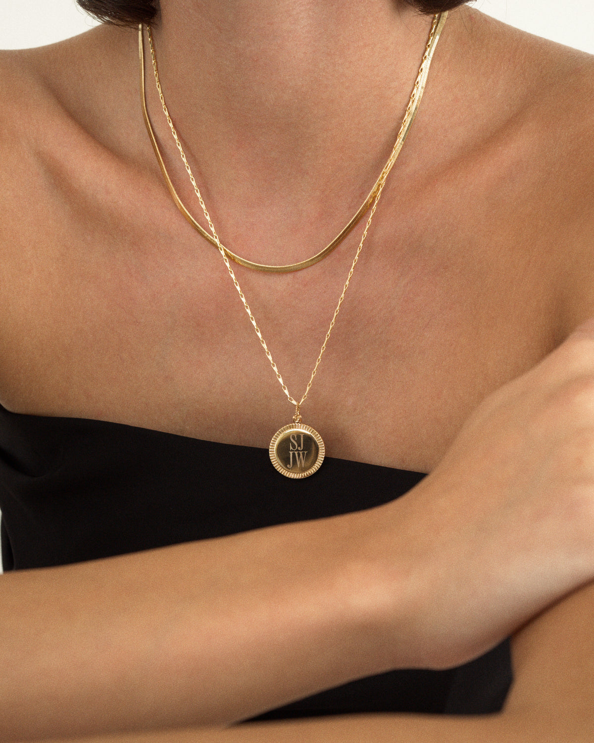 A person wearing two gold necklaces, featuring a Mod + Jo Gia Engravable Charm with the initials SJ JW layered over a flat chain.