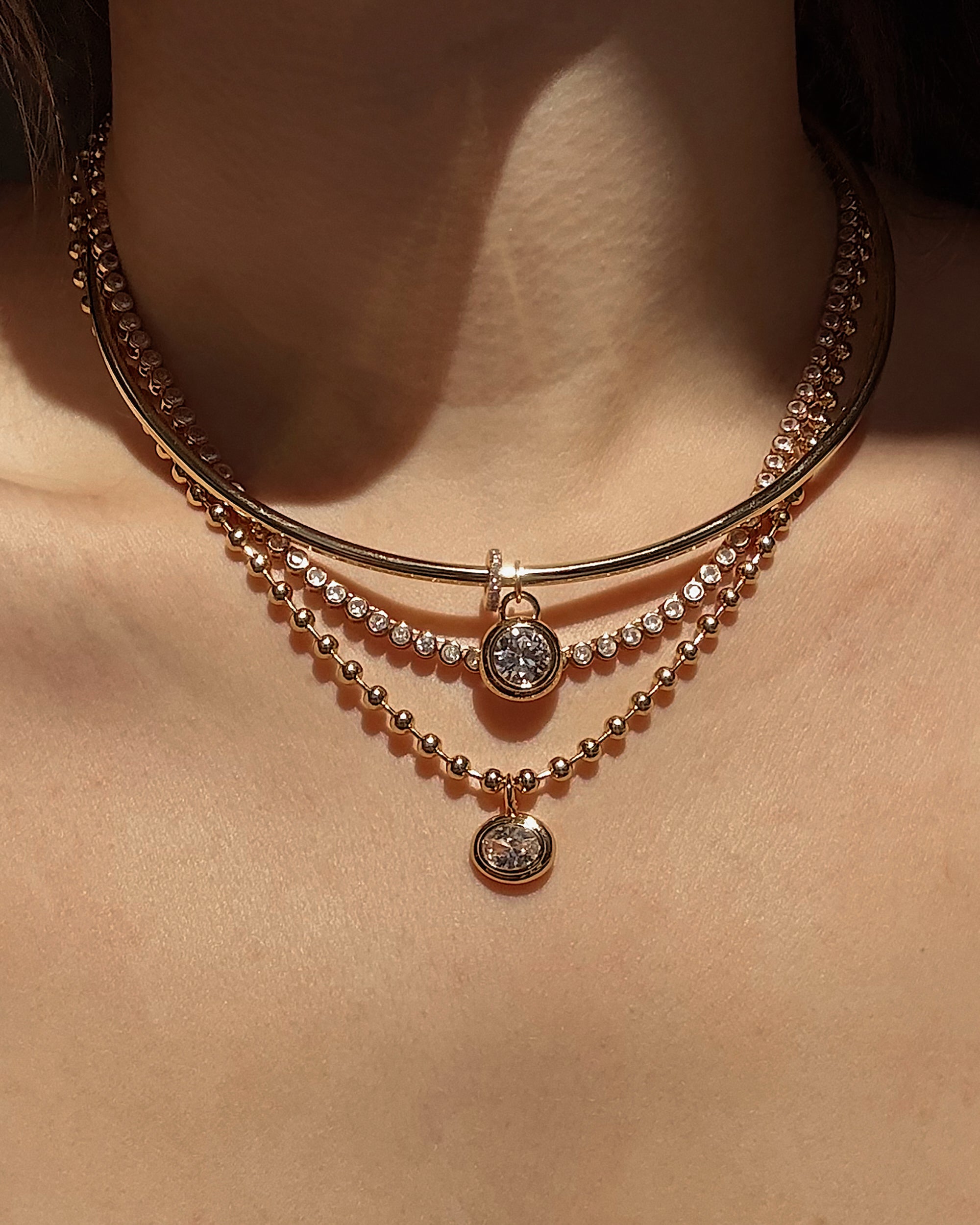 A close-up of a neck wearing three layered Mod + Jo Soren Bezel Pendant Necklaces in 14k gold plate, each with a round pendant and shimmering lab-grown white sapphires catching the light.