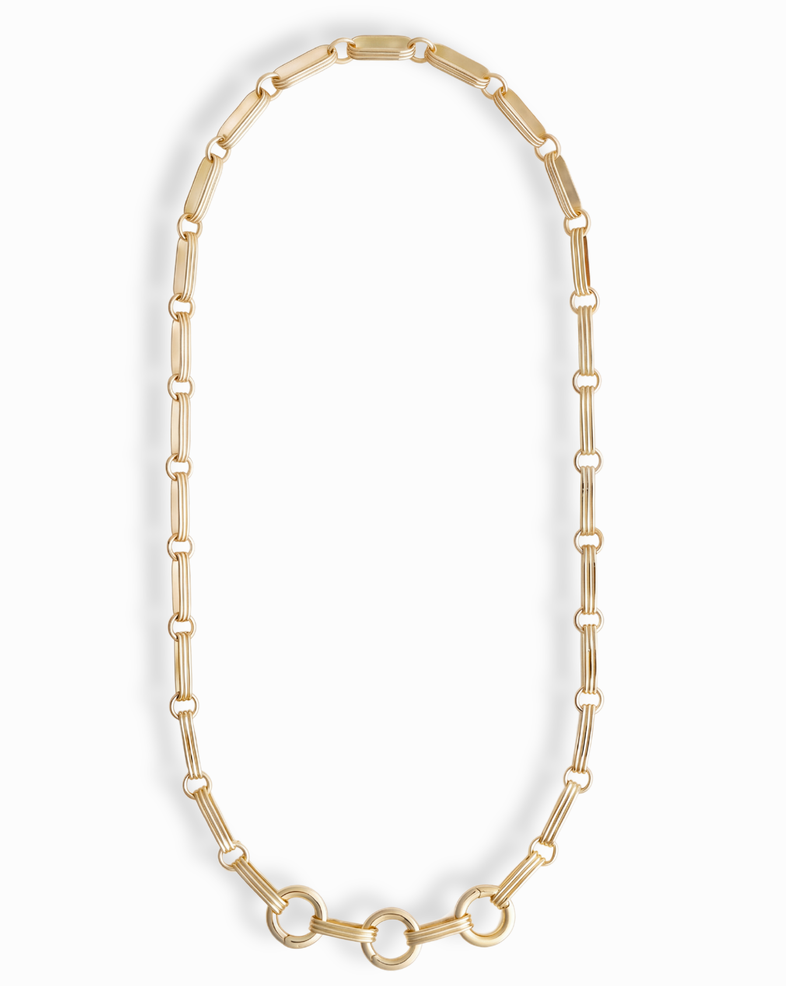 The Jagger Charm Clip Necklace by Mod + Jo features elongated oval links crafted in 14k gold and showcases three larger connected circles at the bottom, elegantly displayed on a white background. This sophisticated necklace seamlessly blends timeless style with contemporary flair.
