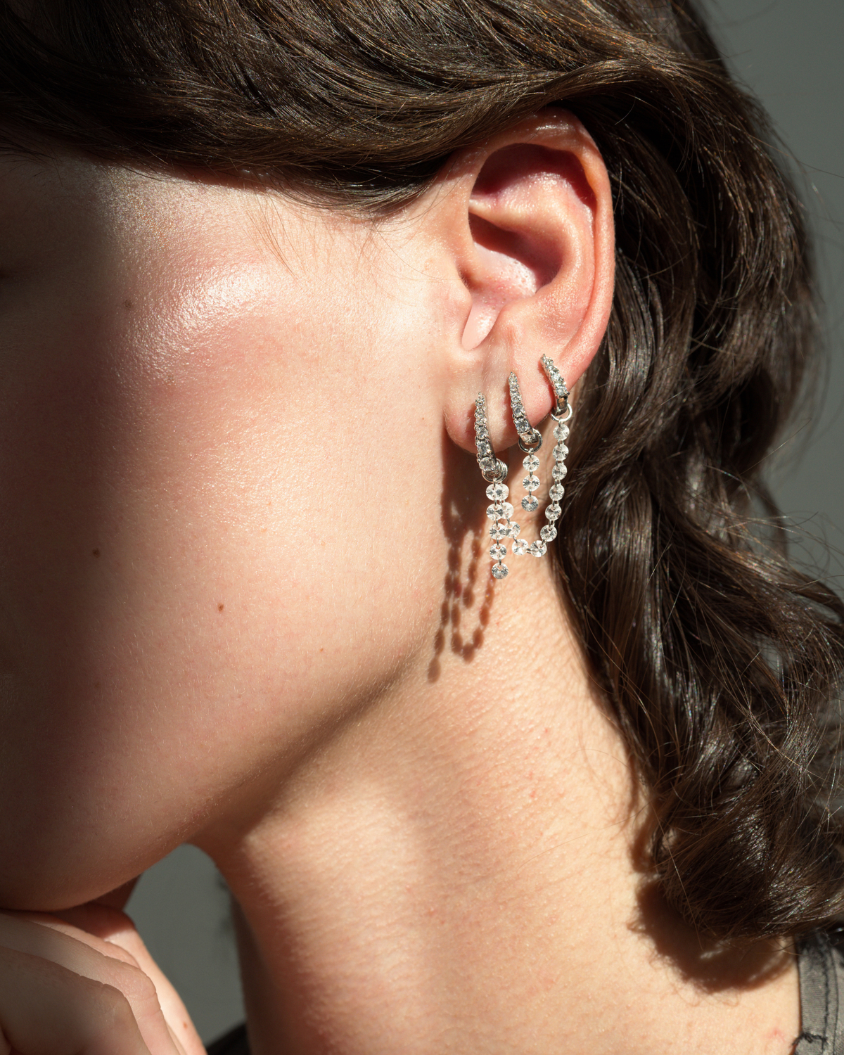 Mod + Jo Iris Sapphire Earring Charms featuring two silver hoop earrings connected by a delicate dangling chain of lab-grown white sapphires worn in a pierced ear.
