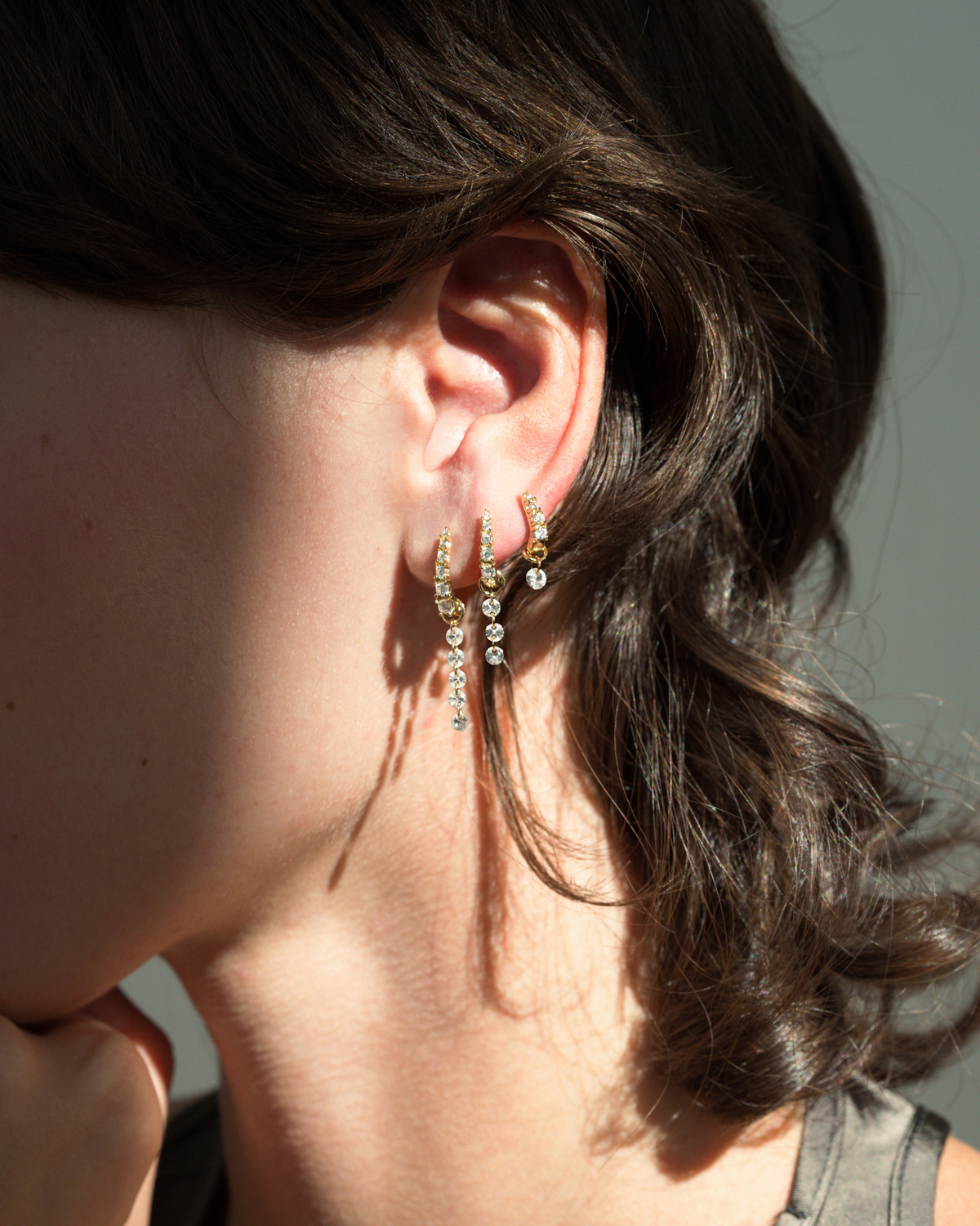 Three 14k gold plated Jules Medium Huggies worn in a row on an earlobe, each featuring small cubic zirconia stones and a dangling charm.
