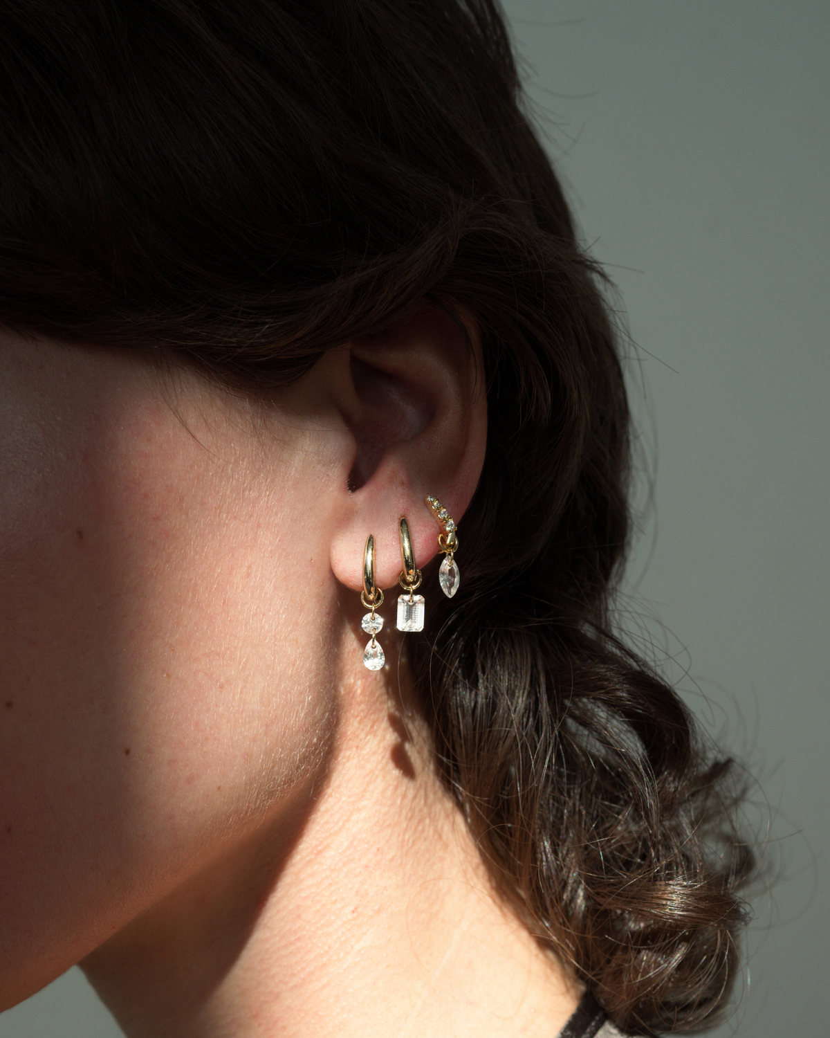 Jules Petite Huggies by Mod + Jo, featuring three 14k gold-plated hoop earrings, each with a dangling cubic zirconia charm in a unique shape.