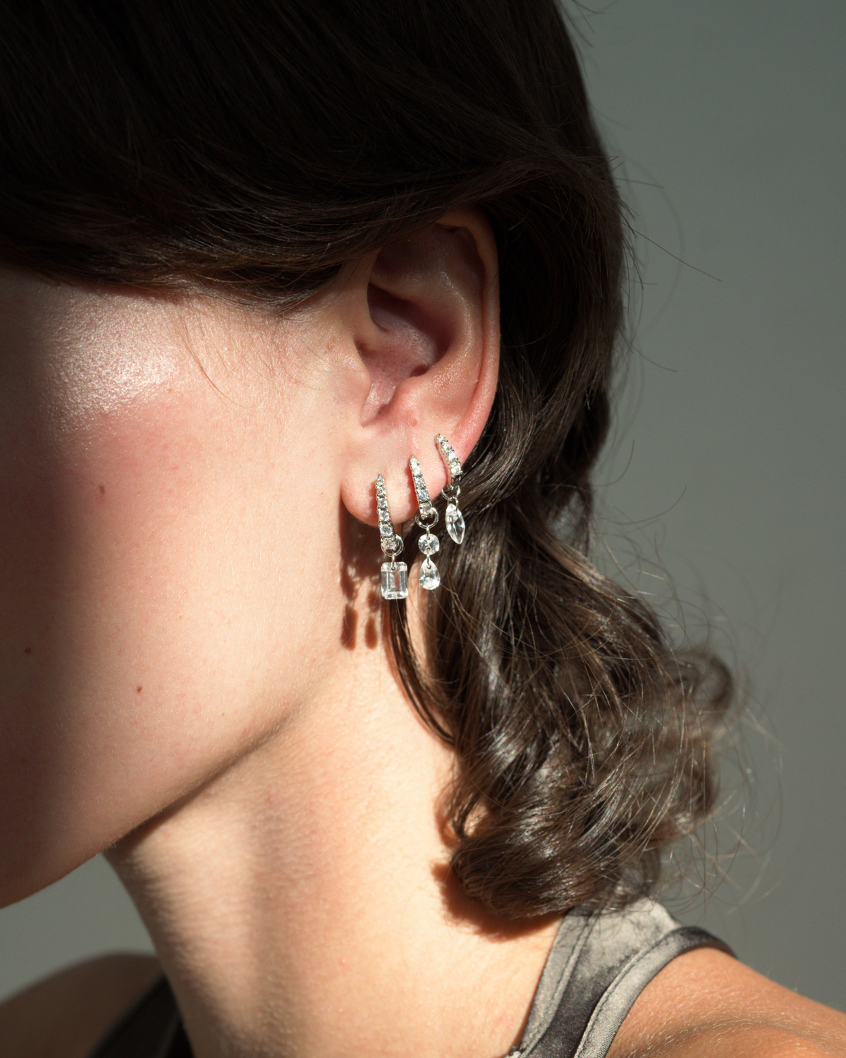 Three Jules Grande Huggies tarnish-resistant silver hoop earrings with hanging cubic zirconia gemstones worn in a single ear.