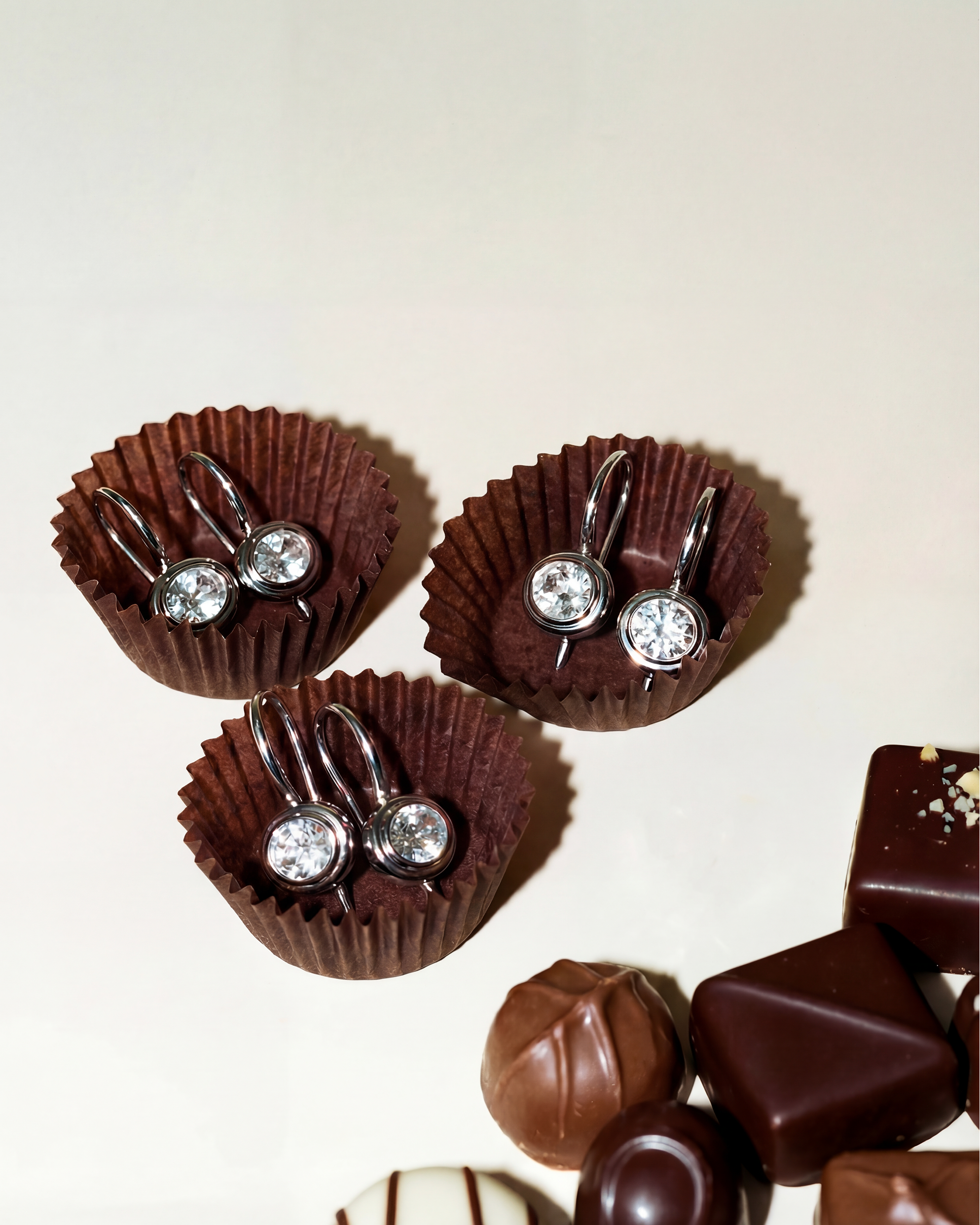 Chocolate earrings with clear gemstones in brown paper cups on a light background