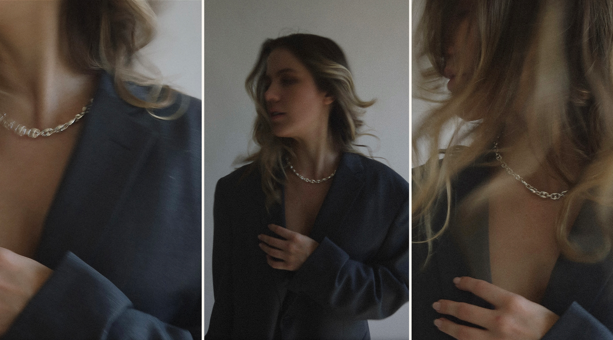 Three blurred images of a person with wavy hair wearing a dark blazer and a chunky silver necklace, photographed from different angles against a plain background. The person’s face is partially obscured.