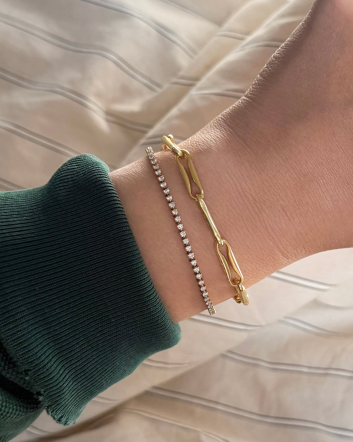 A wrist wearing a nickel-free, gold-plated Molly Elongated Link Chain Bracelet with elongated links alongside a delicate, stone-set tennis bracelet.
