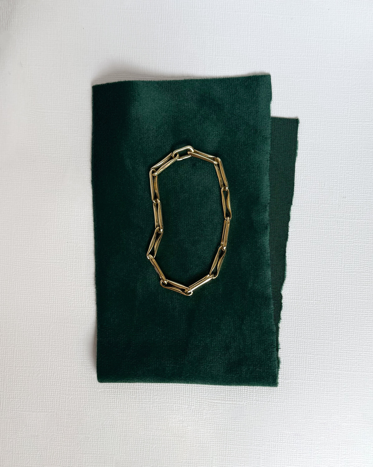 Molly Elongated Link Chain Bracelet centered on a dark green rectangular piece of fabric.