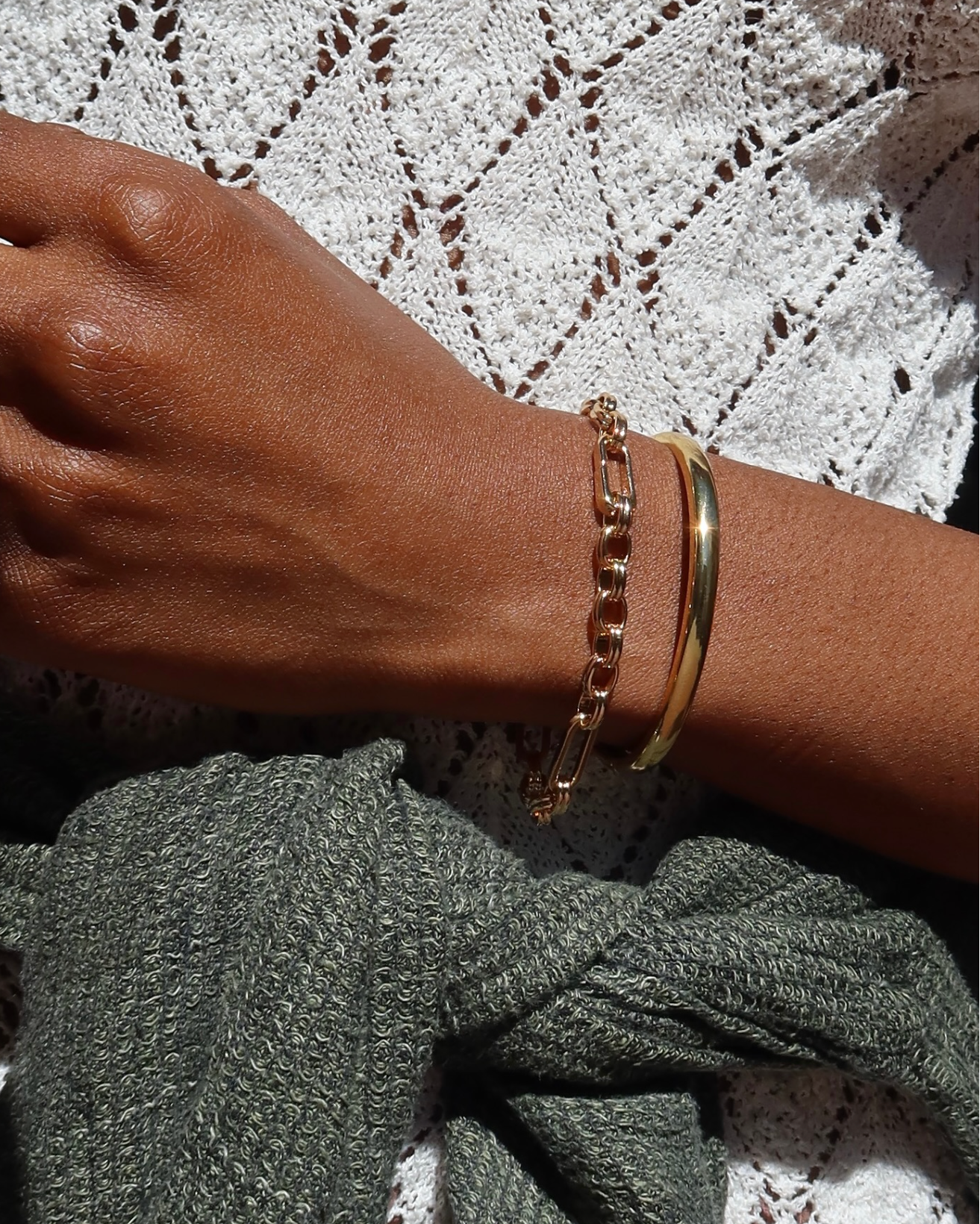 Hand wearing two gold bracelets on a textured background
