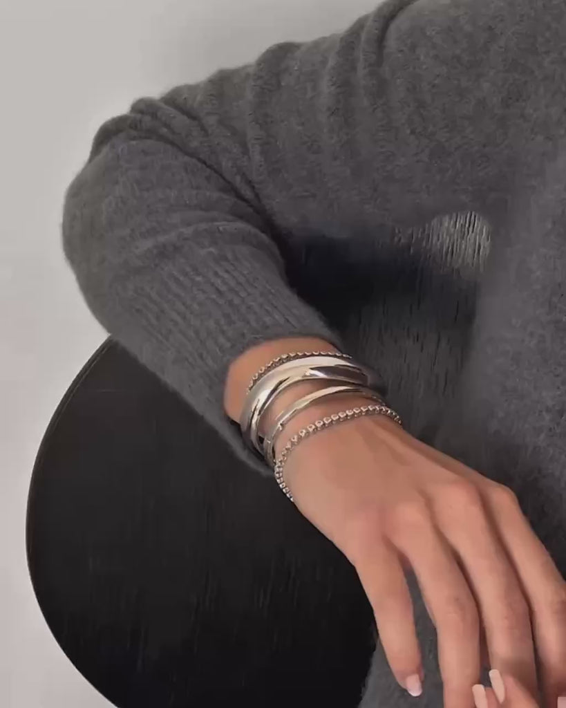 A close of up a woman's arm in a grey sweater with stacked silver bracelets