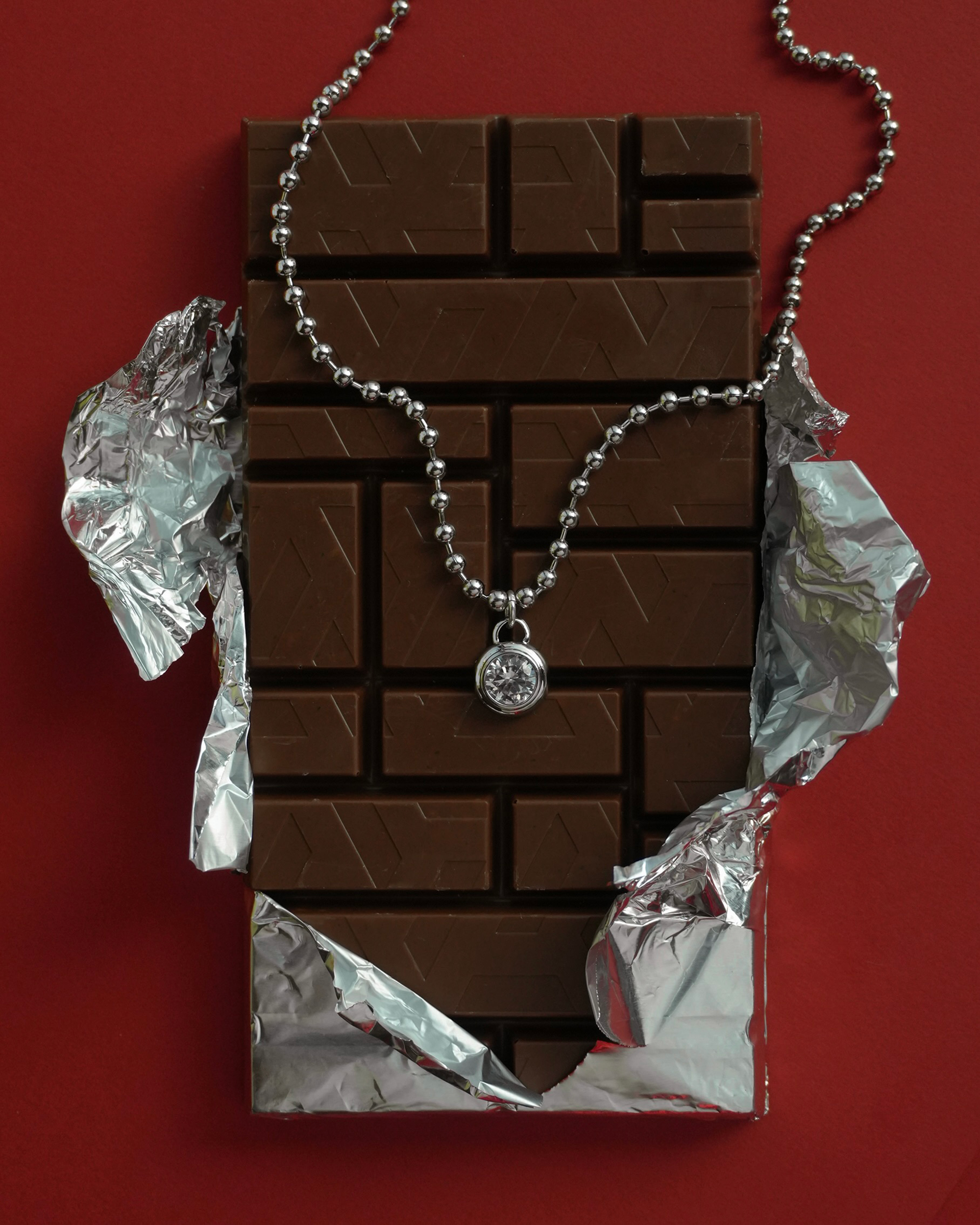 Chocolate bar with a ball chain necklace and round sapphire pendant draped over it on a red background