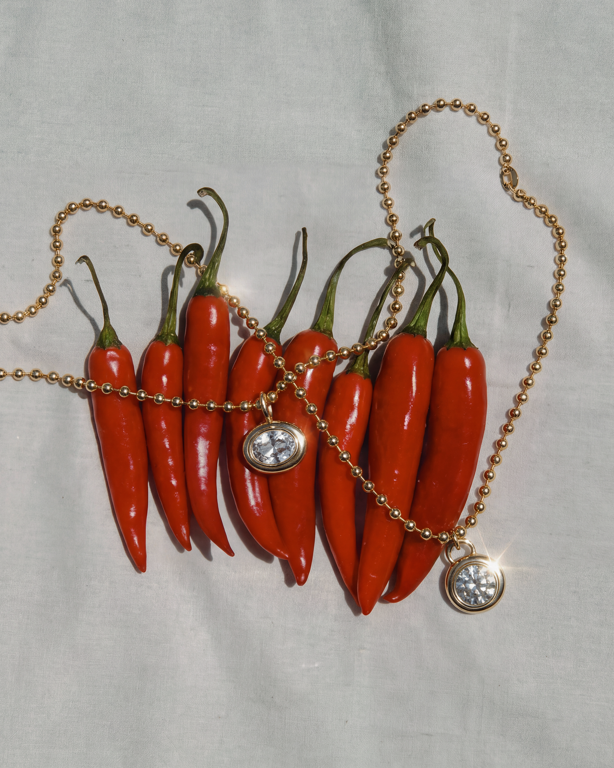 Necklaces with sapphired pendants daped over a bed of red chili peppers on a light gray background