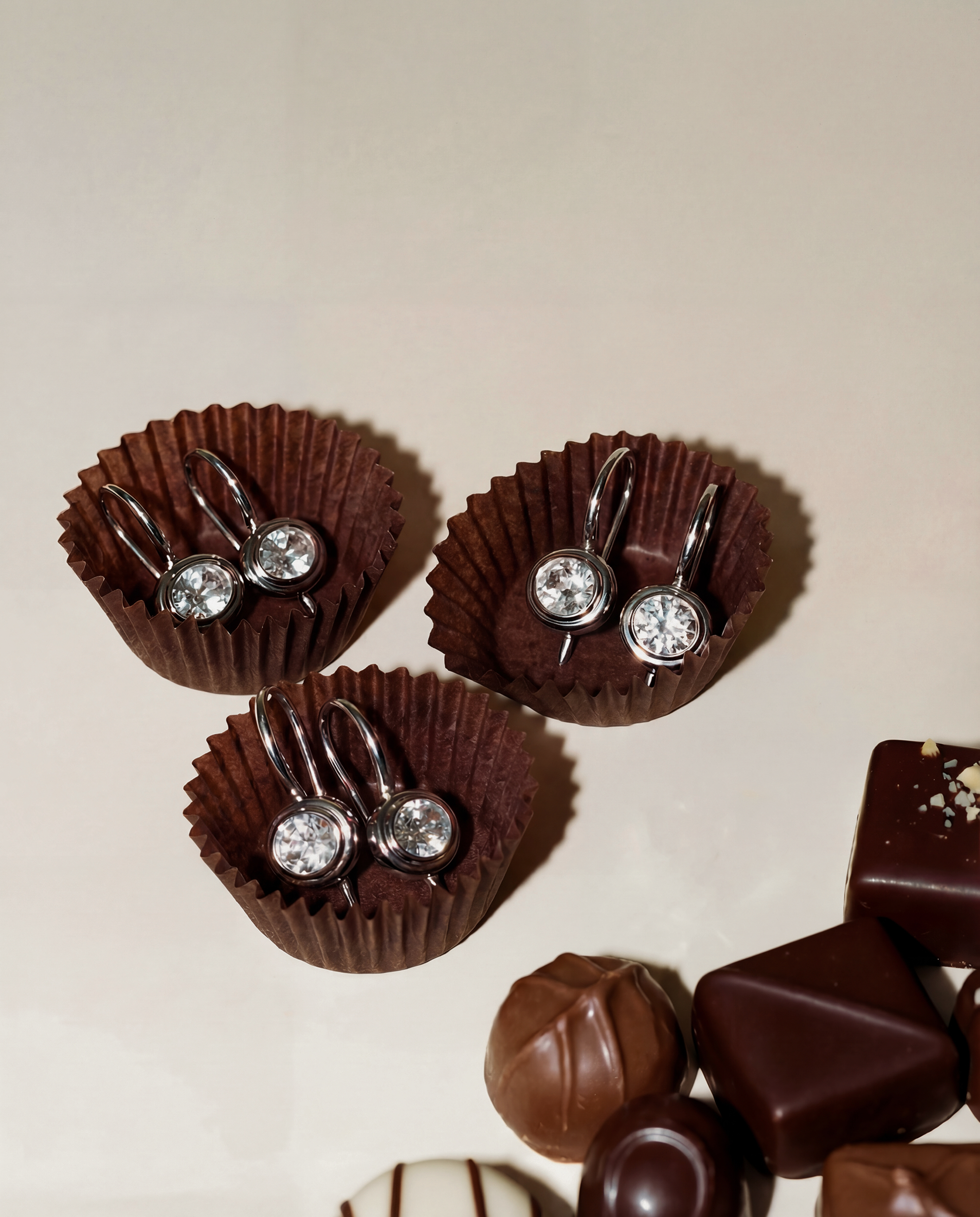 earrings in a chocolate cupcake wrapper with additional chocolates on a beige background